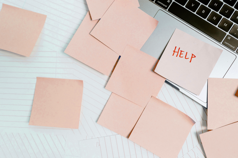 An image of a laptop with sticky notes, one sticky note has the word "Help" written in red ink