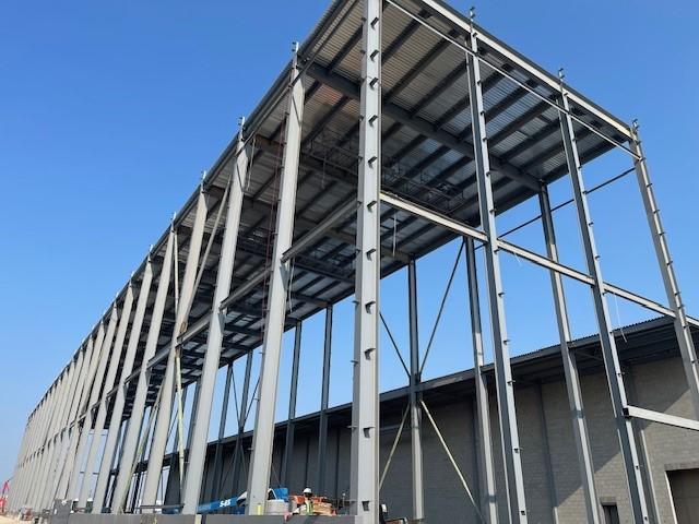 A close-up view of a large steel frame structure with metal decking installed on the roof level.