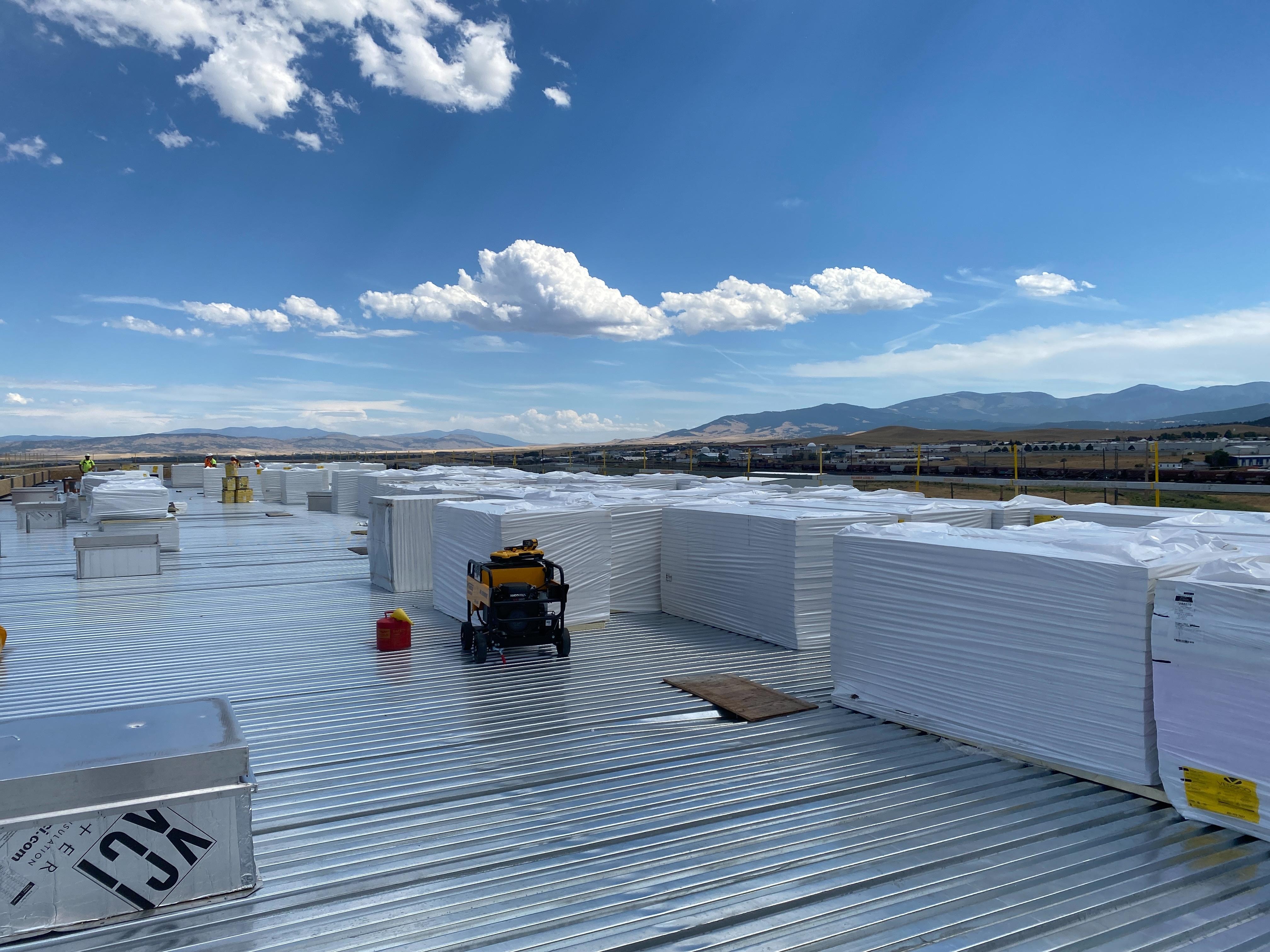 A view of a rooftop with stacks of white roofing insulation material placed on top of corrugated metal decking.