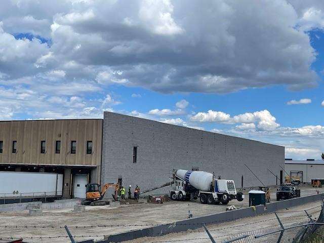 A crane lifts steel beams into place for the warehouse extension, while workers prepare the site below.