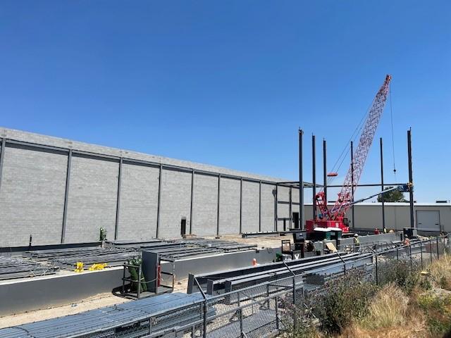 The steel skeleton of the warehouse extension progresses, with construction activity on the ground.