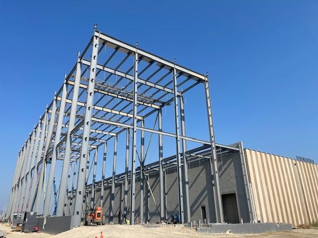 The steel framework of the Montana Department of Revenue's liquor warehouse expansion project is nearly complete, with beams and columns in place and construction equipment visible on site.