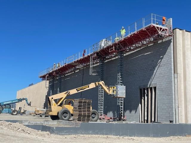 Construction workers are on a raised scaffold working on the masonry wall of the liquor warehouse.