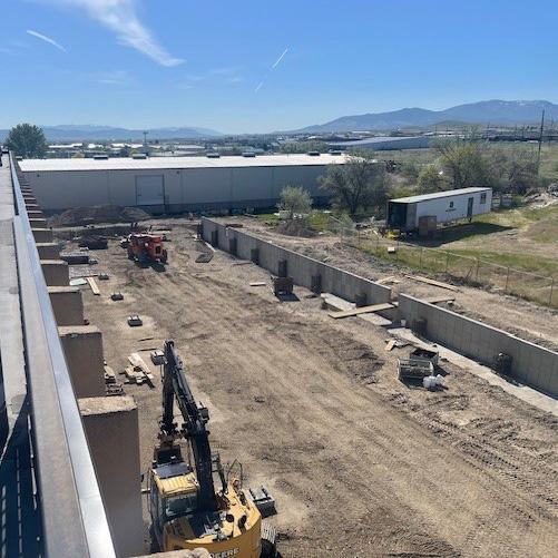 Aerial view of the liquor warehouse construction site with multiple areas of excavation and construction machinery. The area is surrounded by industrial buildings under a clear sky.