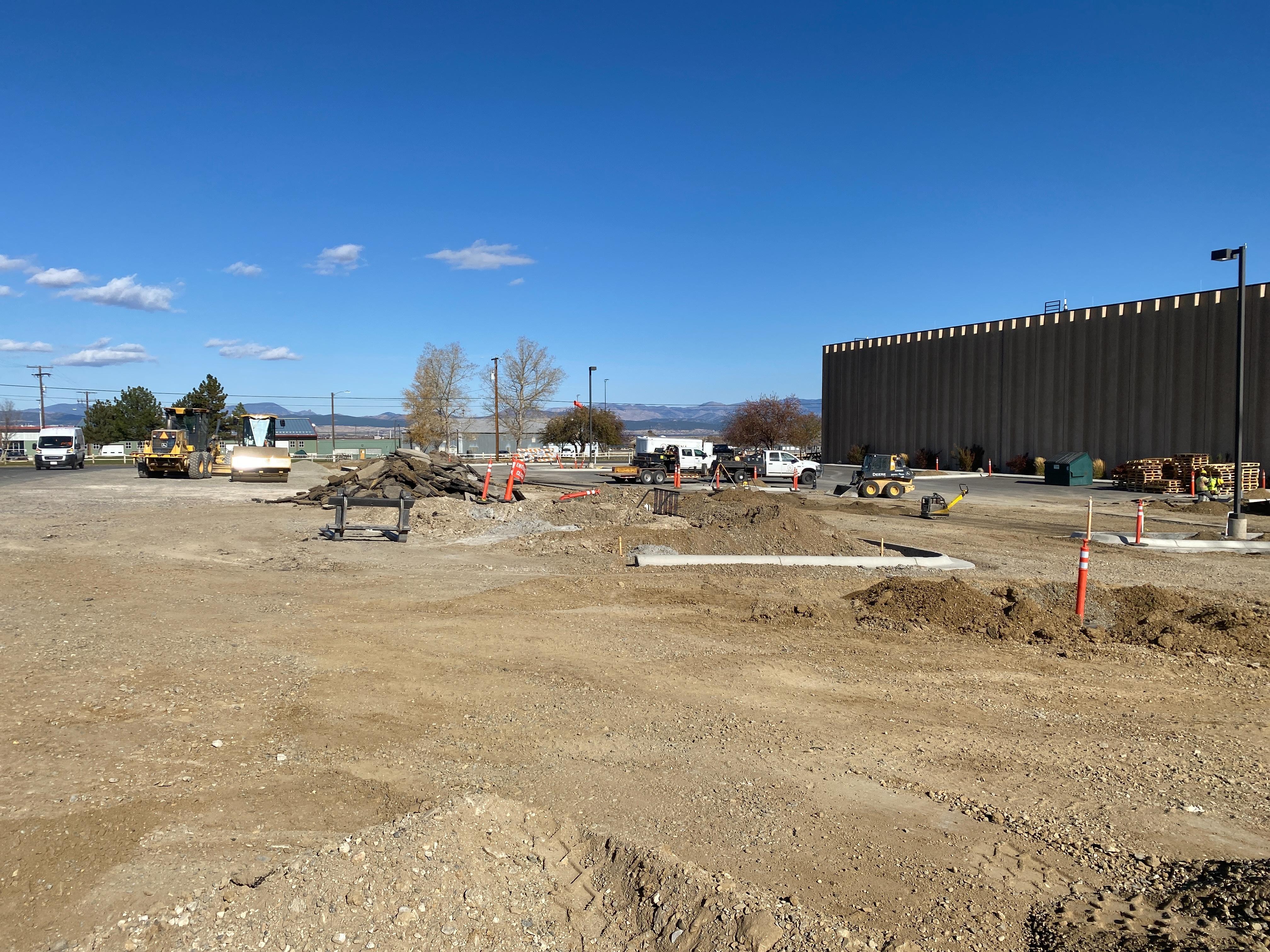 A wide view of a parking lot preparation site, with dirt piles and construction vehicles.