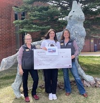 Stella Overstreet, scholarship winner, next to a concrete wolf sculpture, holding a large check.